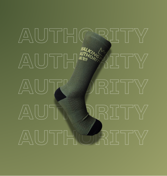 A single dark green crew sock with black heel, toe, and cuff details, featuring the text 'WALKING AUTHORITY'. The sock is displayed diagonally against a matching olive green background with a repeating 'AUTHORITY' watermark pattern.