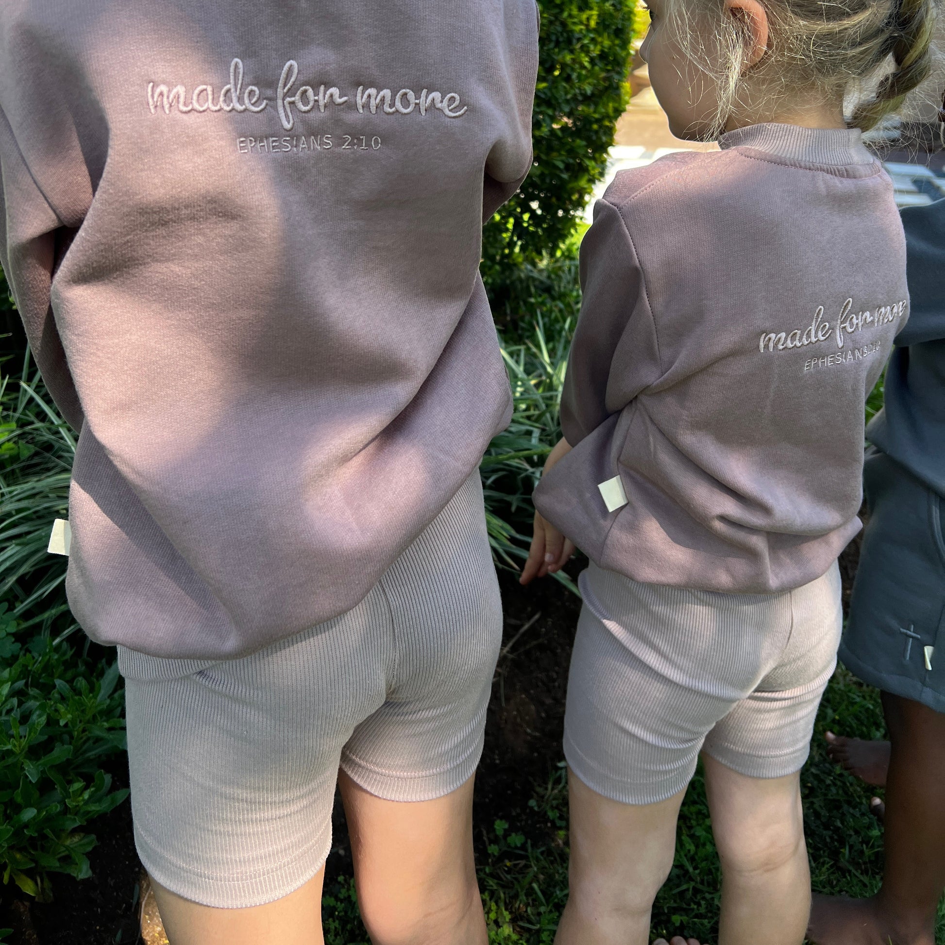 Two children wearing matching sweatshirts with 'made for more' text outdoors.