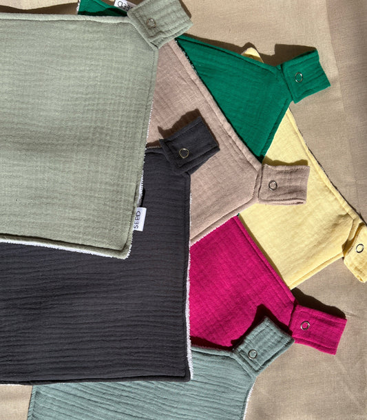 A collection of various colored muslin dummy cloths with clips attached, laid out on a neutral surface.